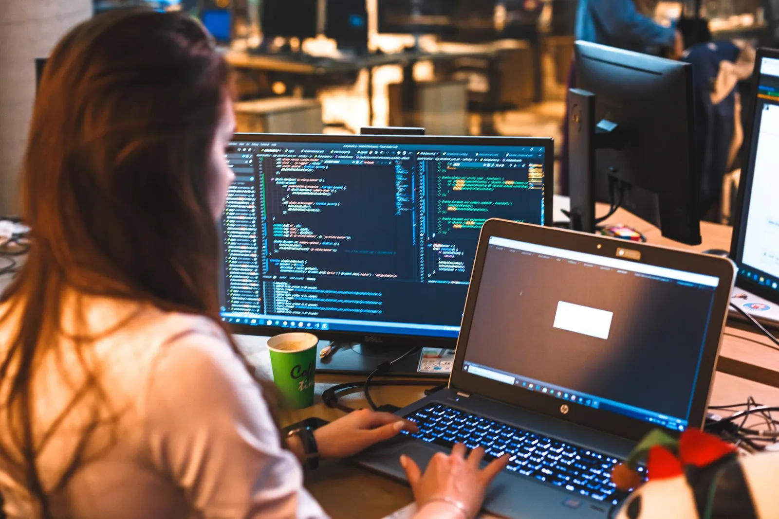 Person arbeitet an Bildschirm und Notebook mit Quellcode